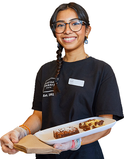 Image of smiling Corner Bakery team member holding desserts